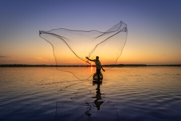 Asian fisherman on wooden boat casting a net for catching freshwater fish in nature