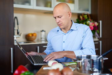 Man in kitchen looking for recipes on his laptop. Cooking in home, online