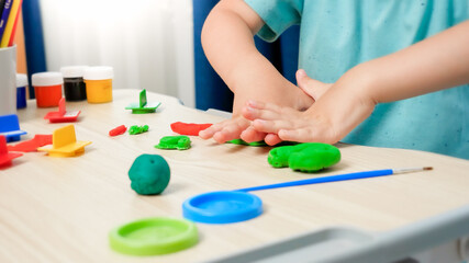 Closeup of little boy using plastic forms for shaping and sculpting toy plasticine or dough. Child hobby on school desk at home