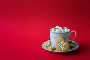 Cup of tasty coffee with marshmallow and heart cookies with Be Mine words on red background. Care, treat and surprise for lovely one on Valentines Day celebration. Cafe drink with copy space.