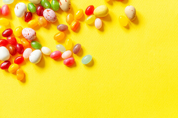 Happy Easter concept. Preparation for holiday. Easter candy chocolate eggs and jellybean sweets isolated on trendy yellow background. Simple minimalism flat lay top view copy space.