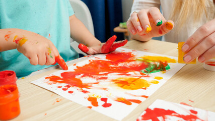 Closeup of adult and child drawing with hands and fingers using colorful paint on white paper. Concept of creative education and art skills development