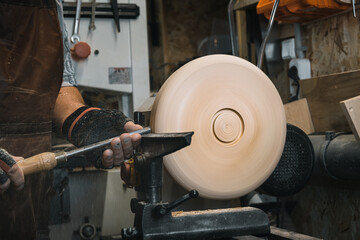 a man in a working apron works on a wood turning lathe. hands hold a chisel. hobby