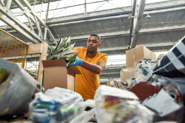 Young man putting packaging into box for reuse