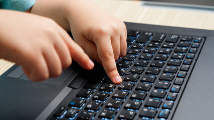 Closeup of child typing and pressing buttons on laptop keyboard. Smart toddler boy learning using computers and laptops.