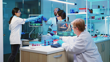 Nurse holding tablet computer with scientific informations while chemist using microscope with chemical test tube near, in lab background at night. Medical science research and development concept