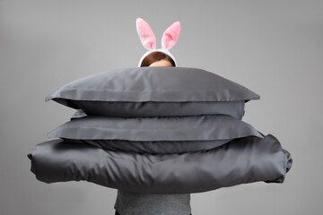 A woman in Easter bunny ears holds a warm duvet and gray feather pillows. Bed linen for sleeping.