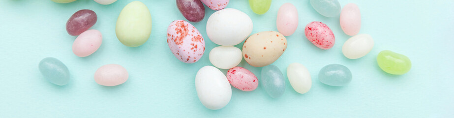 Happy Easter concept. Preparation for holiday. Easter candy chocolate eggs and jellybean sweets isolated on trendy pastel blue background. Simple minimalism flat lay top view copy space. Banner