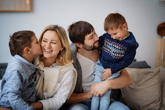 happy young loving caucasian family sitting on sofa and smiling. Son kissing his mom, dad looking with love at his  little boy. Image with selective focus