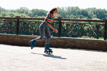 Cheerful beautiful teenage girl rollerblading in the park on a warm summer morning