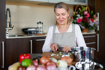 Senior woman in the kitchen cooking, mixing food in a pot.