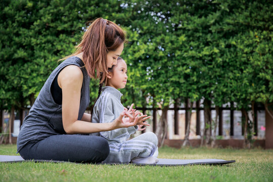 Family Asian Mother Teacher Training Yoga Child Daughter On A Yoga Mat At Home Garden. Family Outdoors. Parent With Child Spends Time Together. Exercise At Home Concept And New Normal.