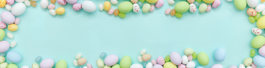 Happy Easter concept. Preparation for holiday. Easter candy chocolate eggs and jellybean sweets isolated on trendy pastel blue background. Simple minimalism flat lay top view copy space. Banner