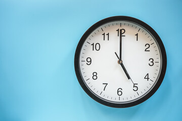 Classic black and white analog clock on blue background at Five o'clock with copy space