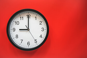 Classic black and white analog clock on red background at Nine o'clock with copy space