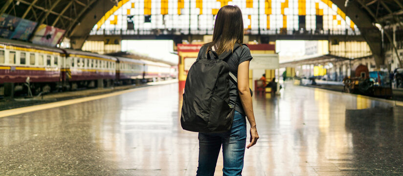 Back view of young asian woman traveler with small backpack on the railway stantion.Waiting for train for transport on holiday trip.Travel concept