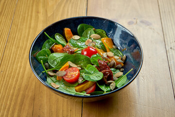 Appetizing salad of baked pumpkin and sun-dried tomatoes in a bowl on a wooden background. Veggie salad