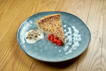 A slice of classic German onion pie with tomato salsa and white sauce. Wooden background.