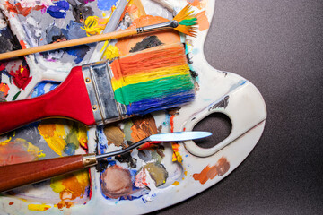 A palette of multi-colored paints with brushes and a palette knife. Black background. Creativity...