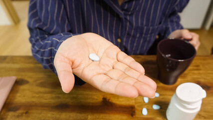 a sky blue pill in a woman's hand and a glass filled with water. a close up of a hand