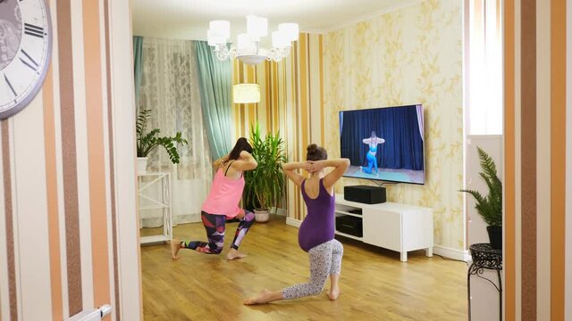 fitness at home. Young woman and teenage girl, in sportswears, watching tutorial video with fitness coach on TV and practicing exercises at home. Online workout, remotely.