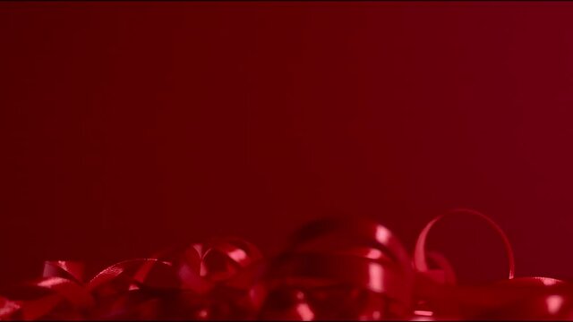 Dark red silky ribbon is falling down on a dark red matte gradient backdrop. Seamless background. New year and Christmas festive mood. Atmospheric Full HD decoration still shot high quality video.