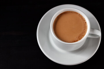 Fototapeta premium Coffee with cream in a white cup on a black wooden table