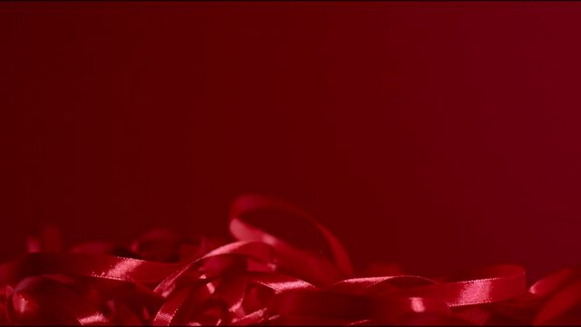 A bunch of red shiny flowing silk ribbons falling down, fluttering on a dark red matte backdrop. Seamless background. Atmospheric New year and Christmas festive mood. Full hd still high quality video
