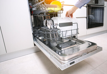 Integrated dishwaher machine loading. Female hand puts plates in dishwasher standing in a modern...
