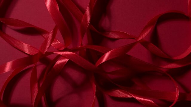 Deep red color silky ribbons are dropping down on a matte ruby backdrop. Atmospheric seamless video background. New year, Christmas festive mood 4k high quality top shot video footage