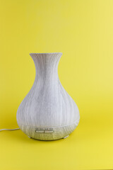 Grey aroma diffuser with steam from water and oil on yellow background