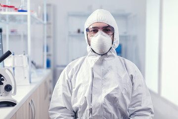 Portrait of tired scientist wearing coverall with protection glasses looking at camera in medicine laboratory. Overworked researcher dressed in protective suit against invection with coronavirus
