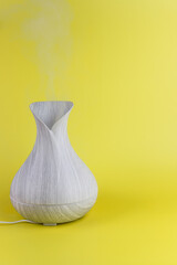 Grey aroma diffuser with steam from water and oil on yellow background