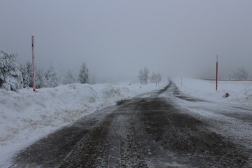 Mit Salz gestreute Landstraße im Winter mit Schnee und Nebel und Bäumen
