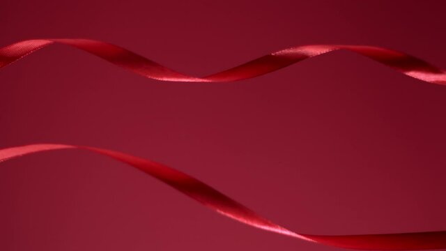 A couple of ruby colored bright glossy ribbons are moving on a matte velvet cherry red backdrop. Atmospheric luxurious video background. Christmas, St. Valentine festive mood. 4k still high quality 