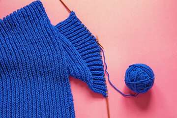 Knitting. Blue scarf with knitting needles and ball of wool on pink background. Copy space