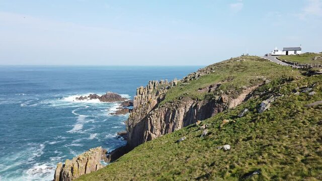 Land's End in Cornwall, England with blue sky and sea waves approaching the coast - Slow pan from right 