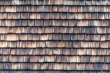 Weathered and faded from the sun, rain and snow wooden shingles that are the facade of an alpine house. Wooden texture in shades of gray and orange.