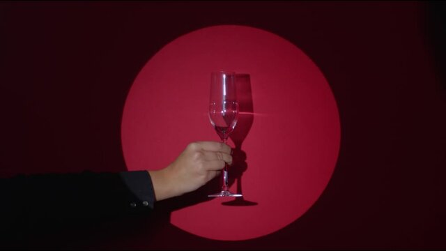 Cherry red matte background. A hand with a champagne glass appears in the spotlight. Another hand in a white glove serving sparkling wine. Confetti flying. 4k high quality still shot video footage.