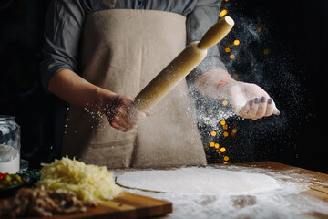 Home Made Pizza Cooking. Woman hands keep rolling pin with flour on dark brown table. Food preparing concept under quarantine due to epidemic.