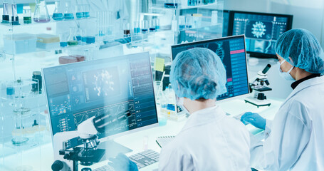 Two female scientists sitting in front of computer screens with coronavirus model and DNA helix....