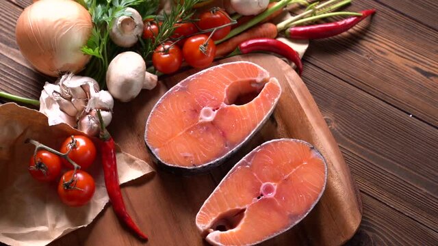 Fresh raw salmon fish steak with herbs and vegetables on wooden background