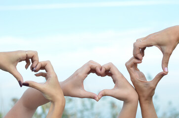 three girls make a heart with their hands on the sky background
