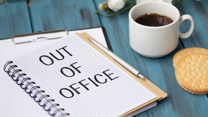Notebook with text Out of Office on wooden office desk table.