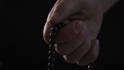 Man's hand with wooden rosary beads touches, black background, close up - Powered by Adobe