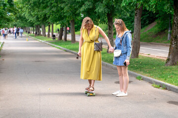 woman standing on longboard supported by her daughter. Woman learning to skateboard outdoors.
