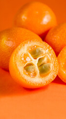 Kumquat cut with seeds against a background of whole kumquats on an orange background. Macro, monochrome, copy space