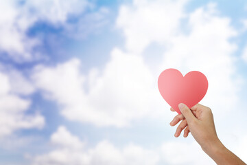 Hand holding paper heart on blue sky background. copy space.