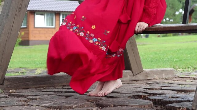 girl in a red ethnic dress sits on a wooden swing in the park. skirt fluttering in the wind