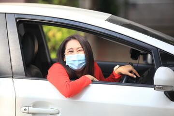  Young woman with medical protective mask on her face is driving a car, she looks into camera and View from outside , Protect yourself.